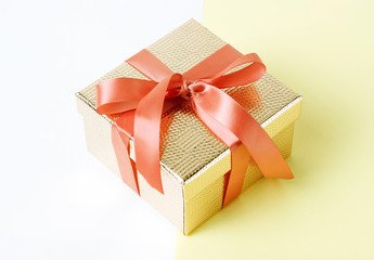 Gold color gift box with pink ribbon on yellow background close-up, copy space.