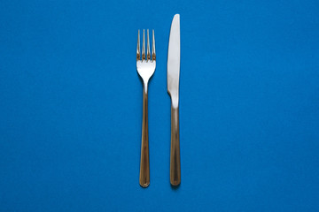 Fork and knife isolated on blue background. Top view.