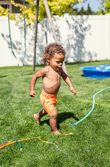 Smiling Cute little boy splashing through the sprinklers in the backyard. African American boy playing in the outdoors on a warm summer day