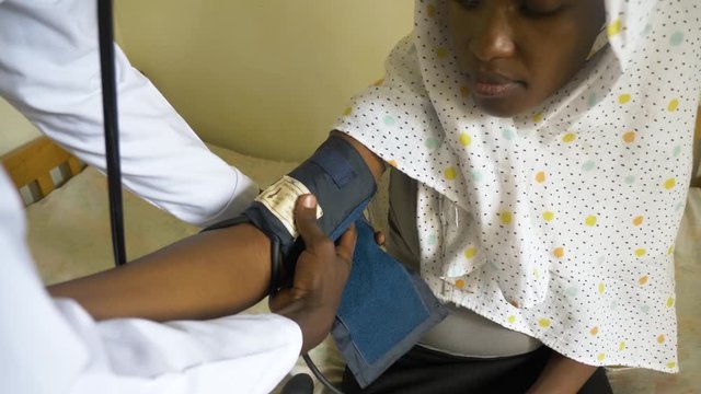 A looking down shot of an African woman getting her blood pressure checked while sitting on a bed in a health clinic.