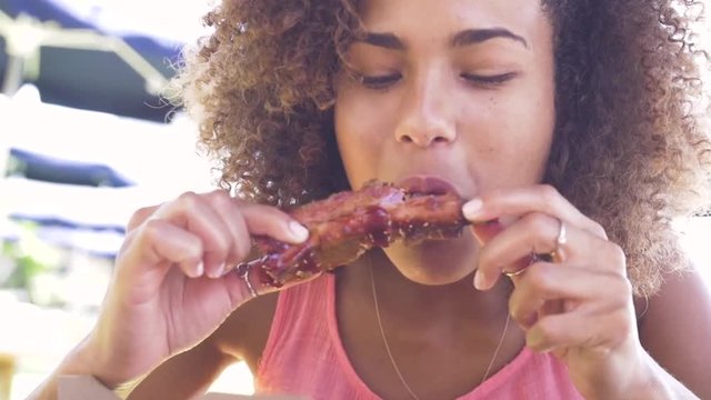 Beautiful ethnic woman eats barbecue ribs.