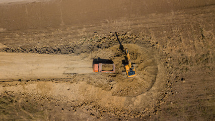 Aerial shot of excavator pours sand into the truck. On the construction site top view. Shooting from the drone.