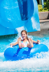Smiling Cute little girl riding down a water slide at a water park with water splashing up. Having fun during summer vacation