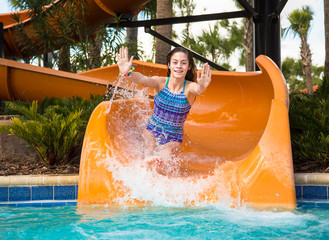 Smiling Cute little girl riding down a water slide at a water park with water splashing up. Having fun during summer vacation