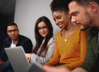 Smiling diverse friends social networking on a laptop computer grouped together reading the latest information on the screen
