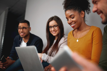 Group of multiethnic friends sitting in line looking at laptop, smiling and reading funny news in social network