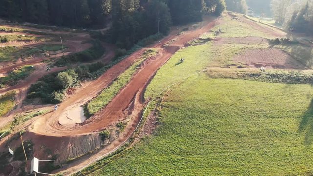 Drone shot of motocross riders riding motorbikes on dirt park track over the left turn and jump fast. Motocross track.