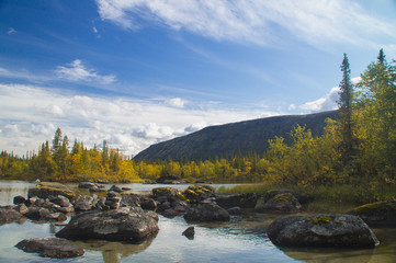 Misty morning on a small mountain lake with a scattering of boulders, reflecting dense clouds, surrounded by autumn forest. Background.