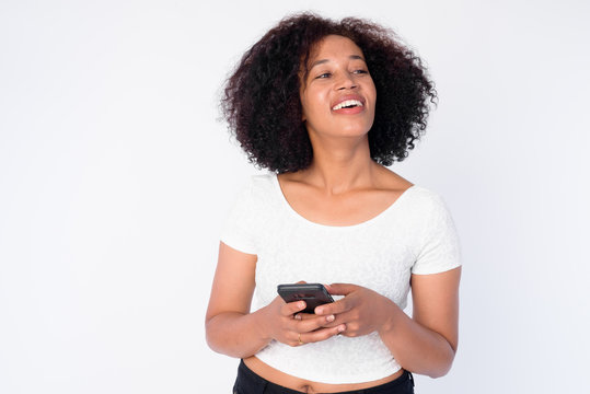 Portrait of happy young beautiful African woman thinking while using phone
