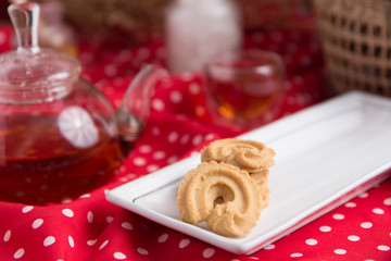 Tea pot and tea cup on wood table with honey and suagr in mag with flower basket on red cloth napkin, with butter cookies and brownies