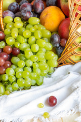 Heap of fresh fruits from new harvest poured out from wicker basket on wooden table covered with linen fabric.