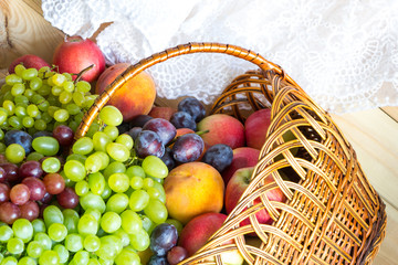 New harvest background. Heap of fresh fruits poured out from wicker basket on wooden table covered with fabric.