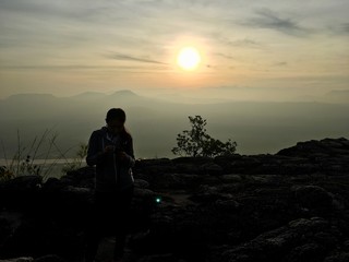 Fototapeta na wymiar Woman standing on the cliff mountain, sunset background