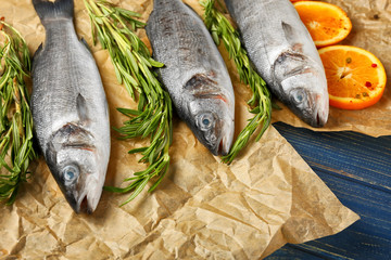 Fresh seabass fish with orange and rosemary on wooden background