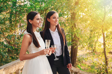Beautiful lesbian couple with glasses of champagne on their wedding day outdoors