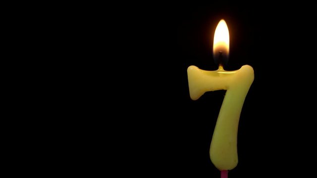 Burning birthday candle isolated on black background with space for text, number 7