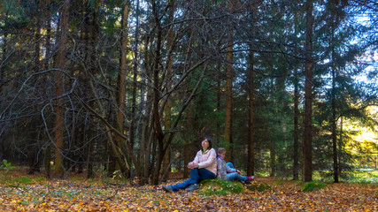 Mom and daughter in the autumn forest sit back to back. Family quarrel and problems of a teenager.