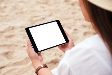 Mockup image of a woman holding a black tablet pc with blank desktop screen while sitting on a beach chair