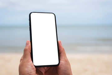 Mockup image of hands holding black mobile phone with blank desktop screen by the sea