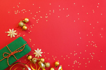 Christmas composition. Green gift box, golden toys on red background with golden confetti. new year concept. Greeting card, xmas celebration 2020. Flat lay, top view, copy space, mockup