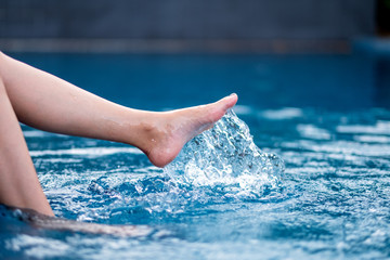 Closeup image of legs and left foot kicking and splashing water in the pool