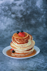 Pancake with orange, strawberry and blueberry on top with maple syrup. Sweet honey pour on pancake layer with grunge background