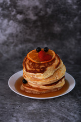 Pancake with orange, strawberry and blueberry on top with maple syrup. Sweet honey pour on pancake layer with grunge background