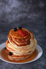 Pancake with orange, strawberry and blueberry on top with maple syrup. Sweet honey pour on pancake layer with grunge background