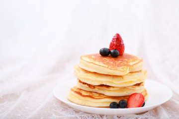 Many layers of pancake with strawberry and  blueberry on white dish  on sweet white cloth background