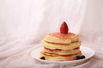 Many layers of pancake with strawberry and  blueberry on white dish  on sweet white cloth background