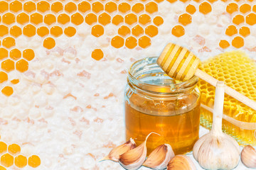 Honey and pieces of garlic on the background of honeycomb. Honey in a glass jar and honeycomb.