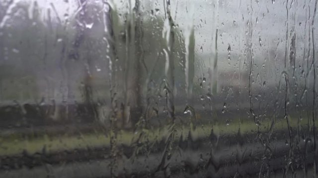 The view from the train window. Outside the window it is raining, water droplets flow down the glass.