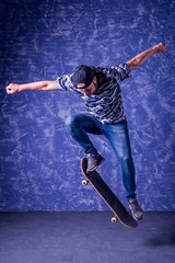 Skateboarder performing a high jump on blue background. Ollie.