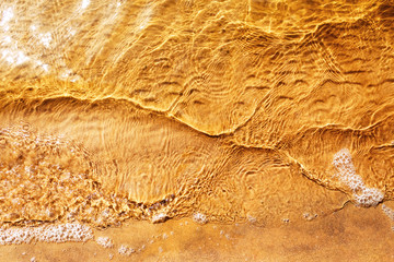 Top view of sand on the beach. Sand texture under the sea water on the beach. Nature background concept. Soft water droplets in the evening sun.