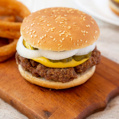 Homemade Mississippi Slug Burger with onion rings on a rustic wooden board, side view. Closeup.