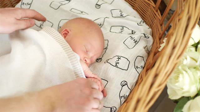 a sleeping newborn baby with a wicker bed is covered with a blanket