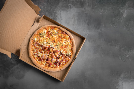 Hot italian pizza in the cardboard box on the grey marble background. Top view and copy space for text
