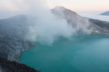 Crater of a volcano with a green sulfuric volcanic lake and volcanic smoke. View of the smoking volcano Kawah Ijen in Indonesia. Mountain landscape