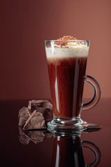 Hot chocolate with whipped cream and pieces of dark chocolate on a brown background.