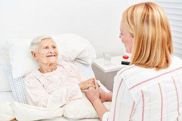 Woman comforts bedridden elderly woman as a patient