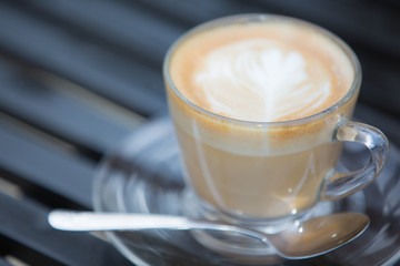 The coffee that is painted in a clear glass is placed on a black iron chair.