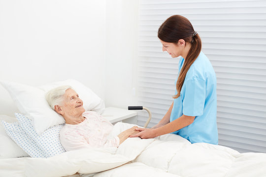 Senior woman is lying in bed talking to nurse