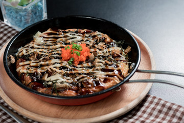 side view of Japanease food, Traditional Okonomiyaki in hot dish topping with orange tobiko on wooden saucer and black background...