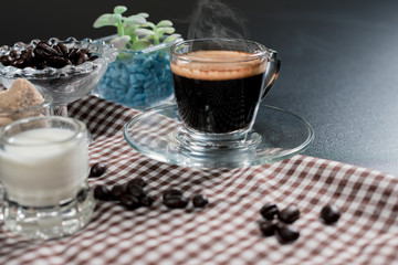 side view a cup of coffee americano in a tranparent cup with coffee beans brown sugar and milk on black table