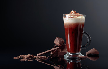 Hot chocolate with whipped cream and pieces of dark chocolate on a black background.