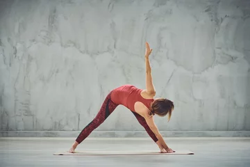 Foto op Aluminium Attractive brunette in red sportswear barefoot doing Triangle yoga posture. © chika_milan