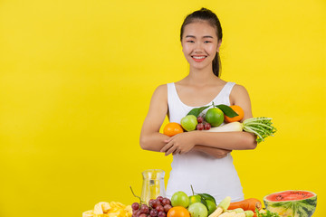 An Asian woman wearing a white tank top. Use both arms to hold various fruits. And there is still left on the table.