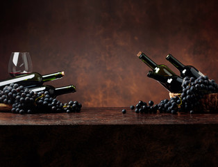 Juicy blue grapes and bottles of red wine on a brown background.