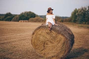 Naklejka na ściany i meble Happy little teen girl. Little girl in a field with hay rolls at sunset