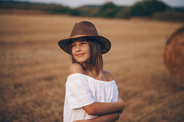 Obraz premium Little girl in a field with hay rolls at sunset